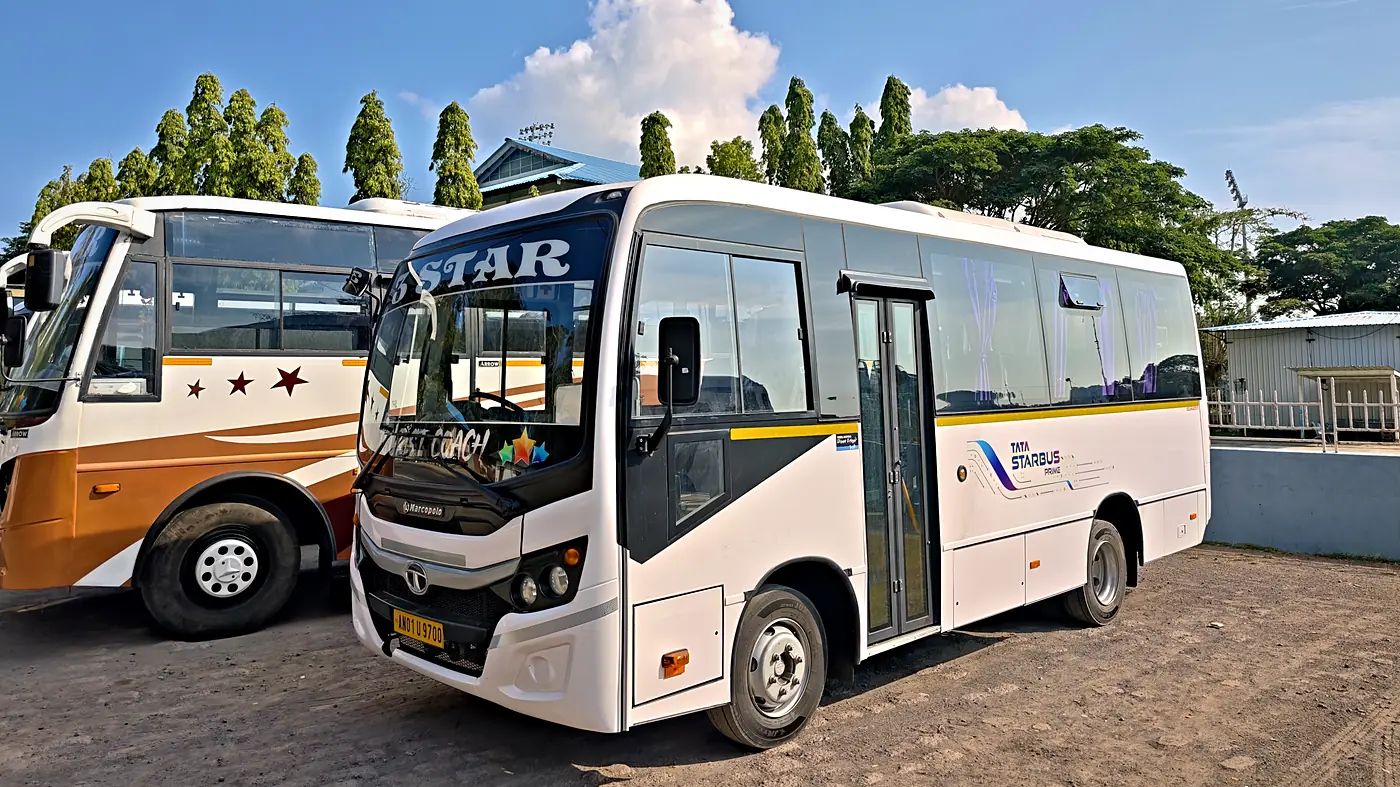 A white 3 Star Tata Starbus mini coach parked beside a white and copper tourist coach under a blue sky