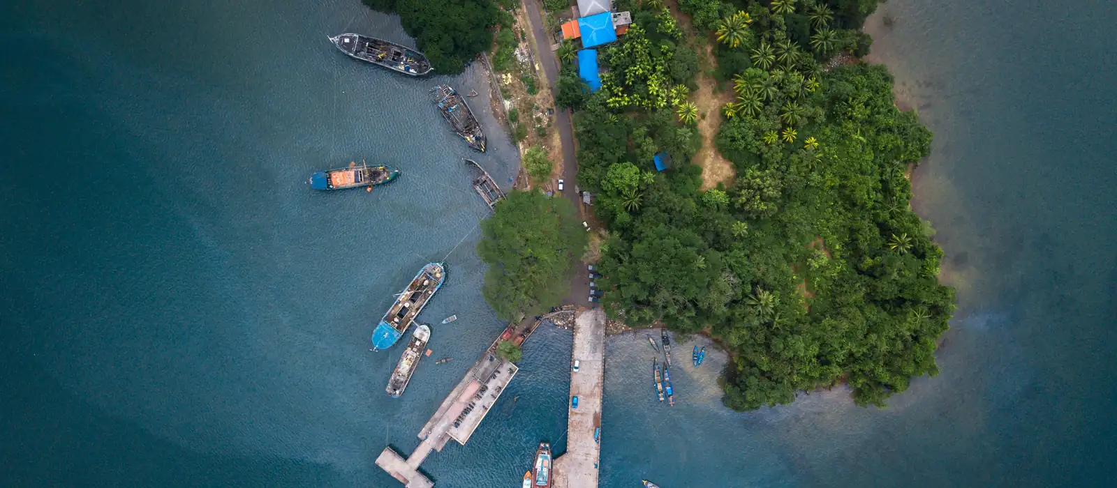 Aerial view of a jetty with fishing boats beside a green Andaman island